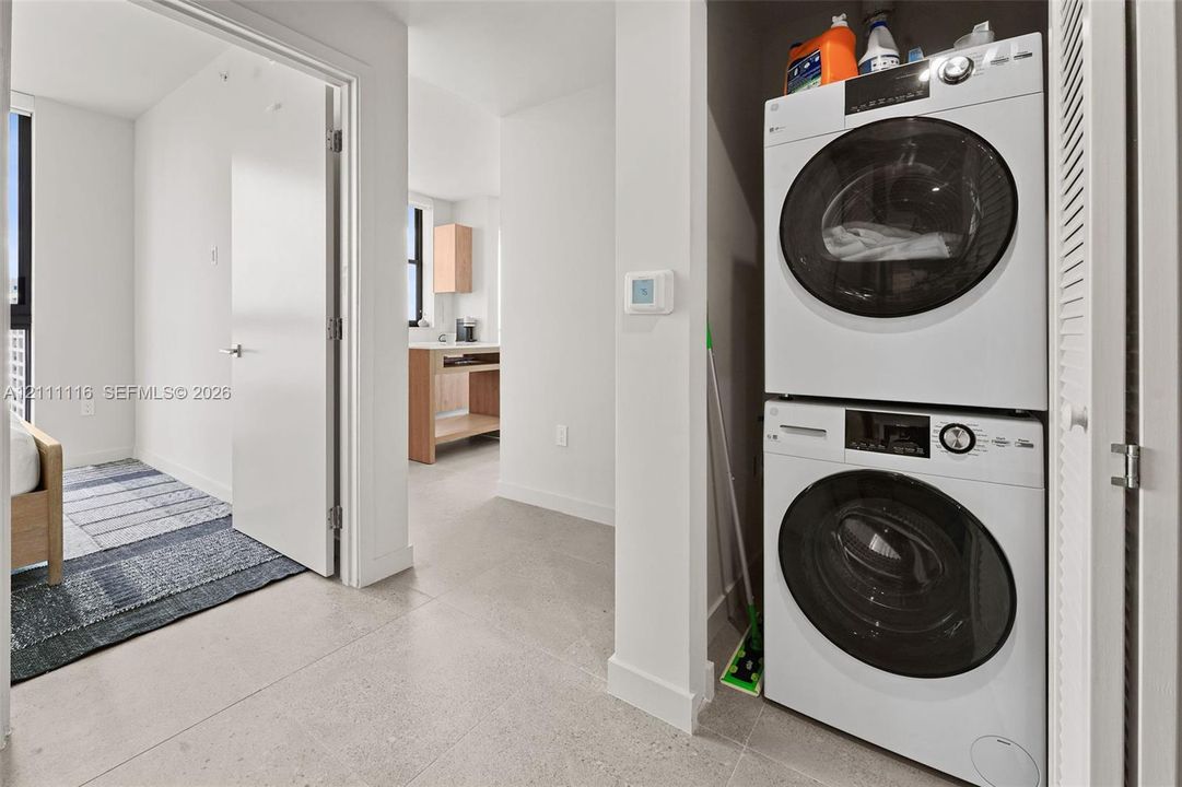 Stacked white front-loading laundry units with integrated digital controls and neutral-tone tile flooring