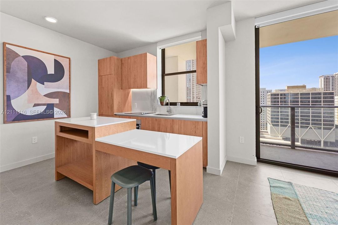 Kitchen featuring wood-finish cabinetry, white countertops, a built-in island with integrated seating, recessed lighting, and a sliding glass door leading to a balcony