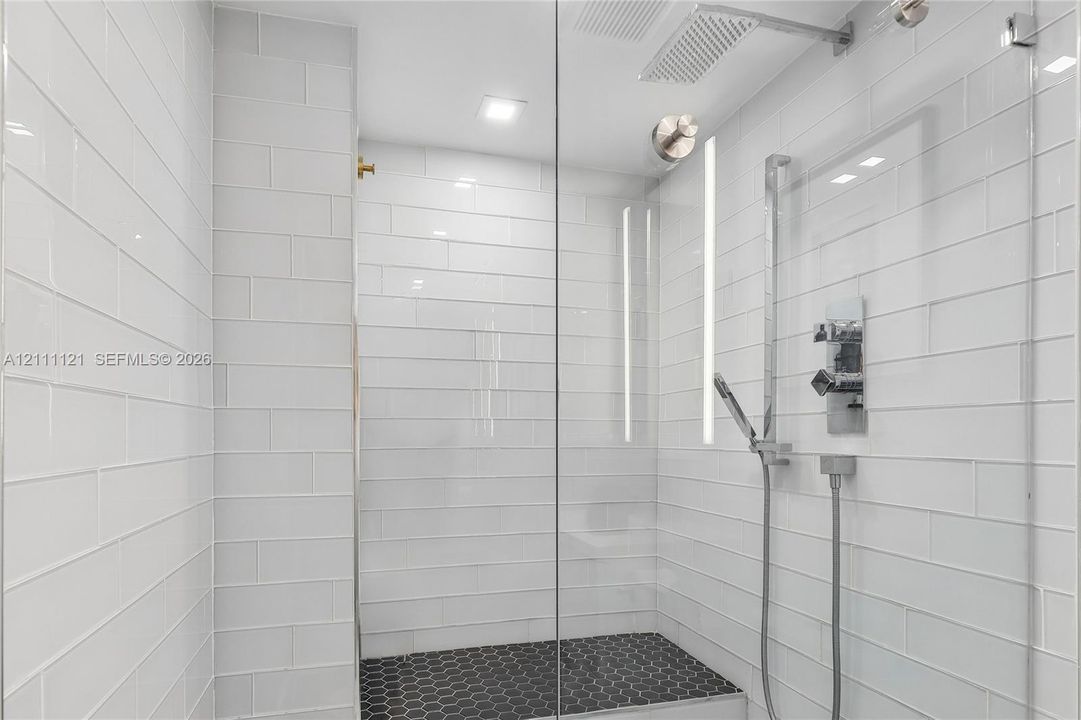 Walk-in shower featuring white subway wall tile, black hexagonal floor tile, a glass enclosure, a rainfall showerhead, and a handheld shower fixture