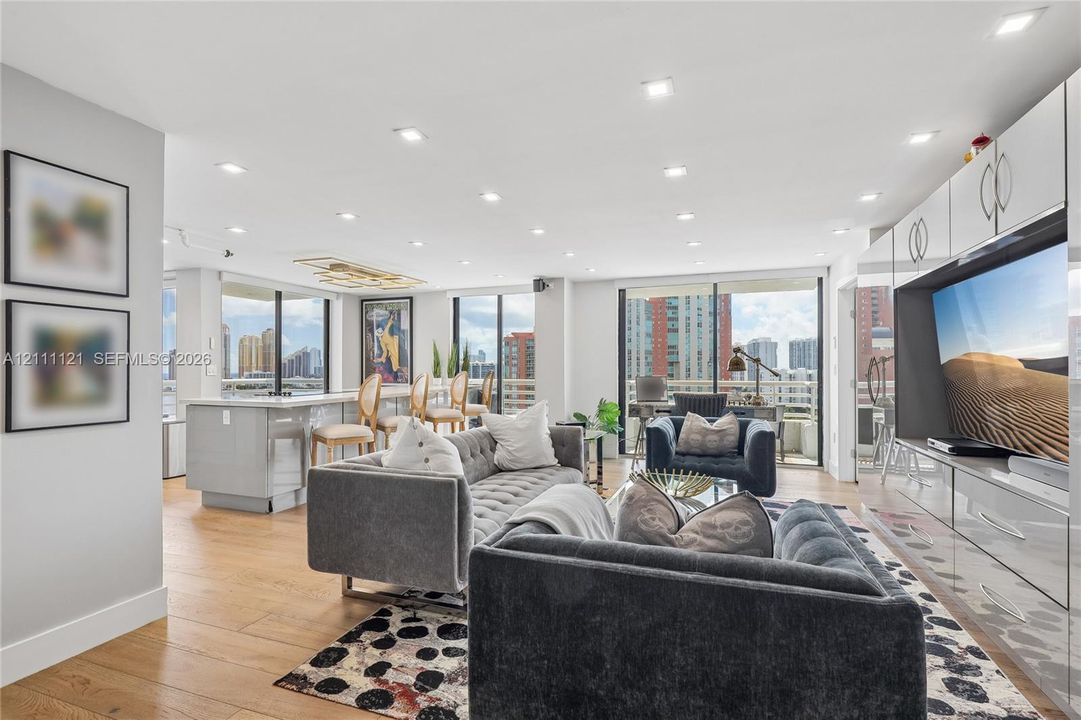 Open-concept main living area featuring wood-finish flooring, recessed lighting, floor-to-ceiling glass sliding doors, and custom built-in white cabinetry with integrated media storage