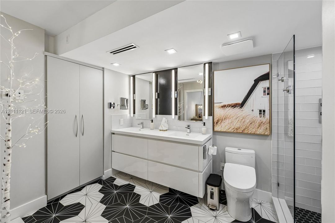 Floating double vanity with integrated sinks, recessed LED vanity lighting, floor-to-ceiling cabinetry, geometric tile flooring, and glass-enclosed shower with white subway tile surround