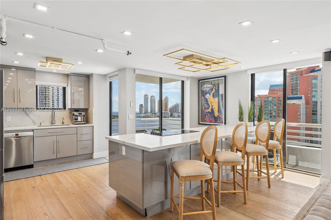 Contemporary kitchen featuring wood-finish flooring, high-gloss cabinetry, a quartz waterfall island, recessed lighting, and floor-to-ceiling glass sliding doors