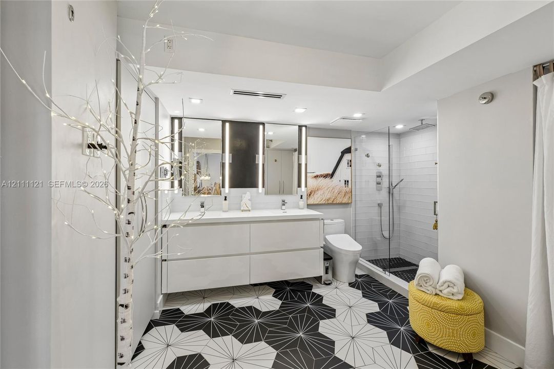 Floating double vanity with integrated sinks, geometric patterned floor tiling, frameless glass-enclosed shower with wall-mounted fixtures, and dual vertical-light vanity mirrors