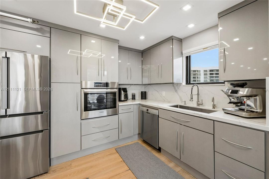 Contemporary kitchen featuring high-gloss cabinetry, stone-patterned backsplash, stainless steel appliances, wood-finish flooring, and a geometric LED ceiling fixture