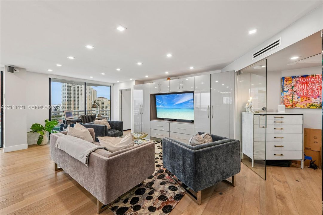 Open-concept interior featuring light wood-finish flooring, recessed lighting, floor-to-ceiling glass enclosure, and high-gloss built-in cabinetry with integrated media center