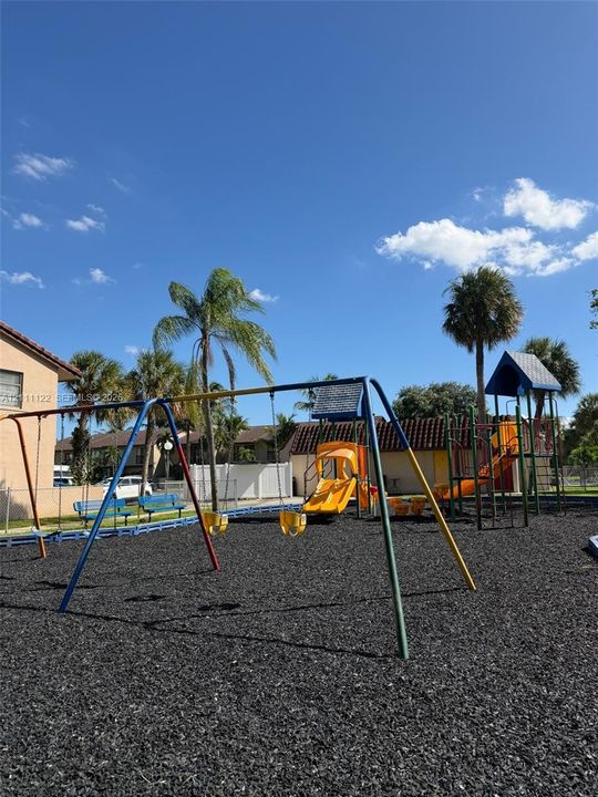 Outdoor recreational area featuring a swing set, multi-level climbing structure with slides, and rubber mulch surfacing