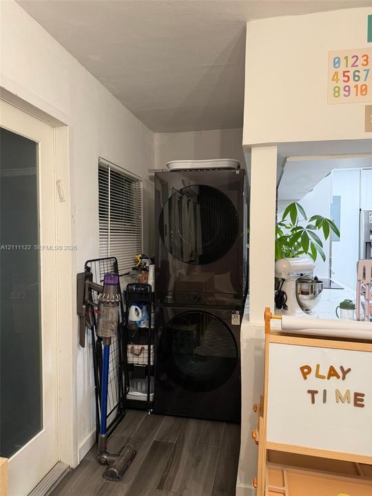 Laundry alcove featuring a stacked high-capacity washer and dryer, wood-finish flooring, and horizontal window blinds