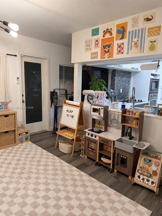Open-concept interior featuring wood-finish flooring, a pass-through window with a serving ledge, an exterior door with a glass inlay, and contemporary multi-bulb ceiling lighting