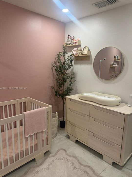Room featuring an accent wall in a muted rose tone, neutral light-finish wood-tone built-in cabinetry, large-format tile flooring, a circular wall-mounted mirror, and recessed lighting