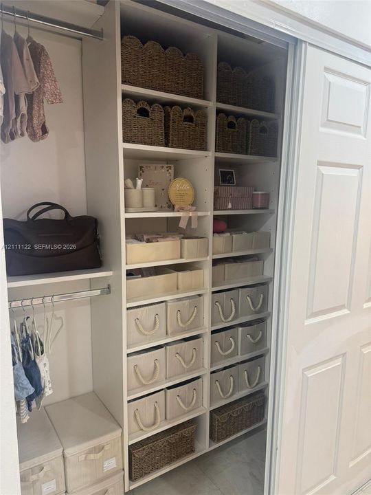 Customized built-in closet featuring white shelving, multiple storage compartments, and dual metal garment rods behind sliding panel doors
