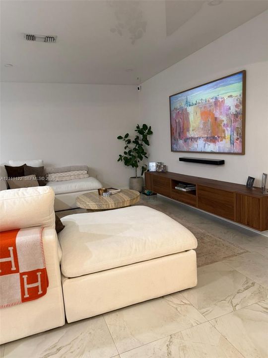 Wall-mounted walnut media console, recessed lighting, and large-format stone tile flooring