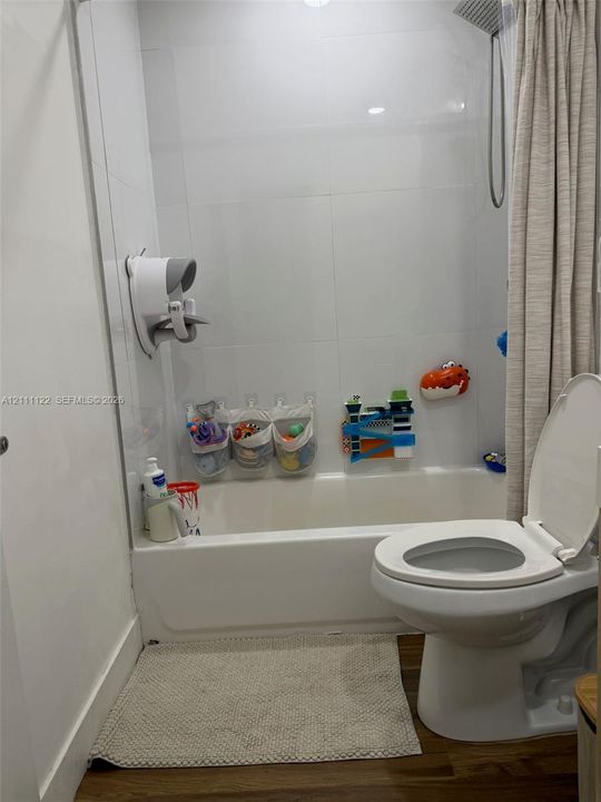 Bathroom featuring a white porcelain tub, full-height white wall tiling, a rainfall showerhead, and wood-finish flooring