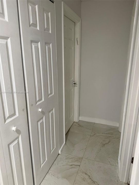 Neutral-toned interior featuring large-format tile flooring, white paneled doors, and double-door closet storage