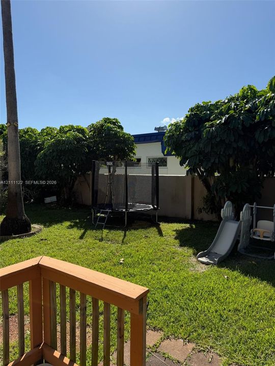 Backyard featuring a grass lawn, wooden deck, mature trees, and a perimeter masonry wall