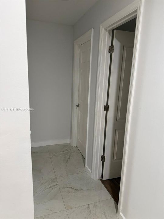 Large-format, stone-finish floor tiling with neutral veining, paired with white interior doors featuring classic panel detailing and polished metal hardware