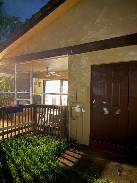 Exterior patio area featuring a screened enclosure, wood-style railing, ceiling fan, and six-panel solid door
