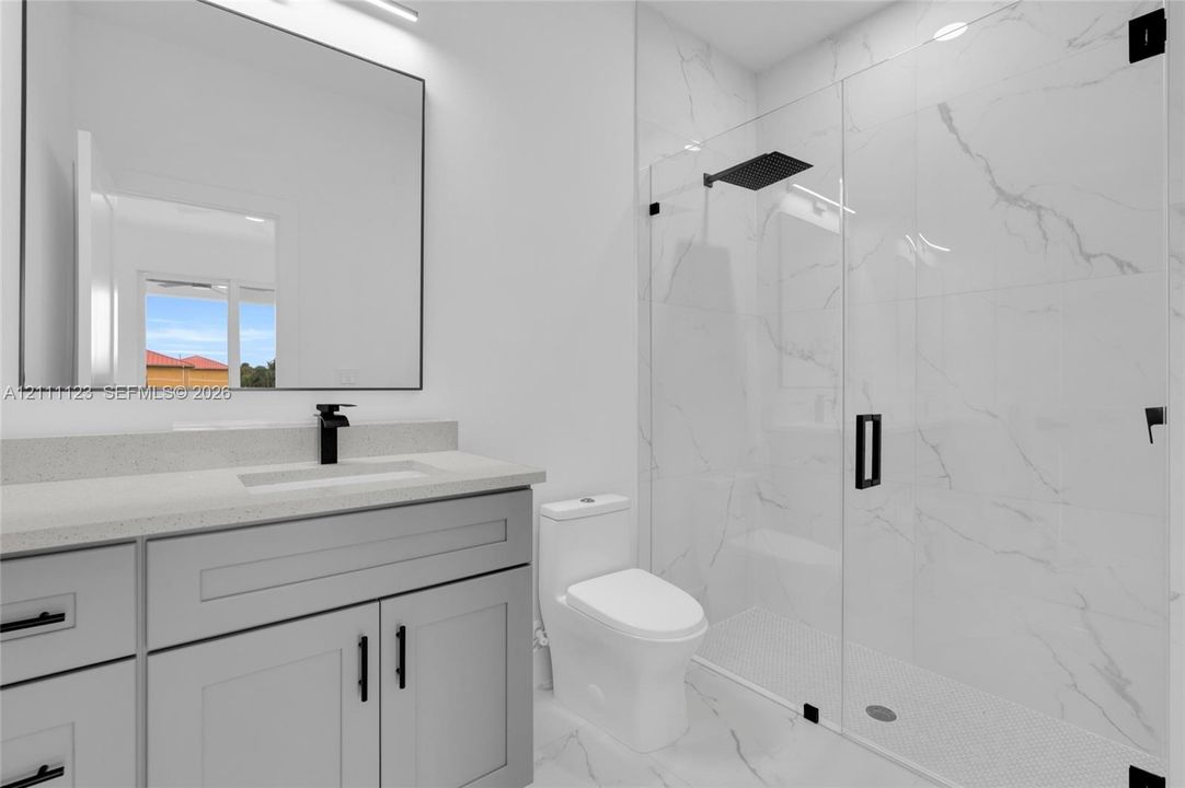 Primary bath with glass-enclosed shower, quartz-topped gray vanity, and black fixtures.