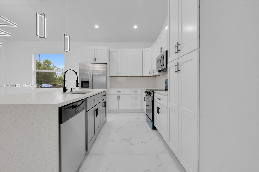 Island with sink, black faucet, and stainless steel dishwasher alongside off-white cabinetry.