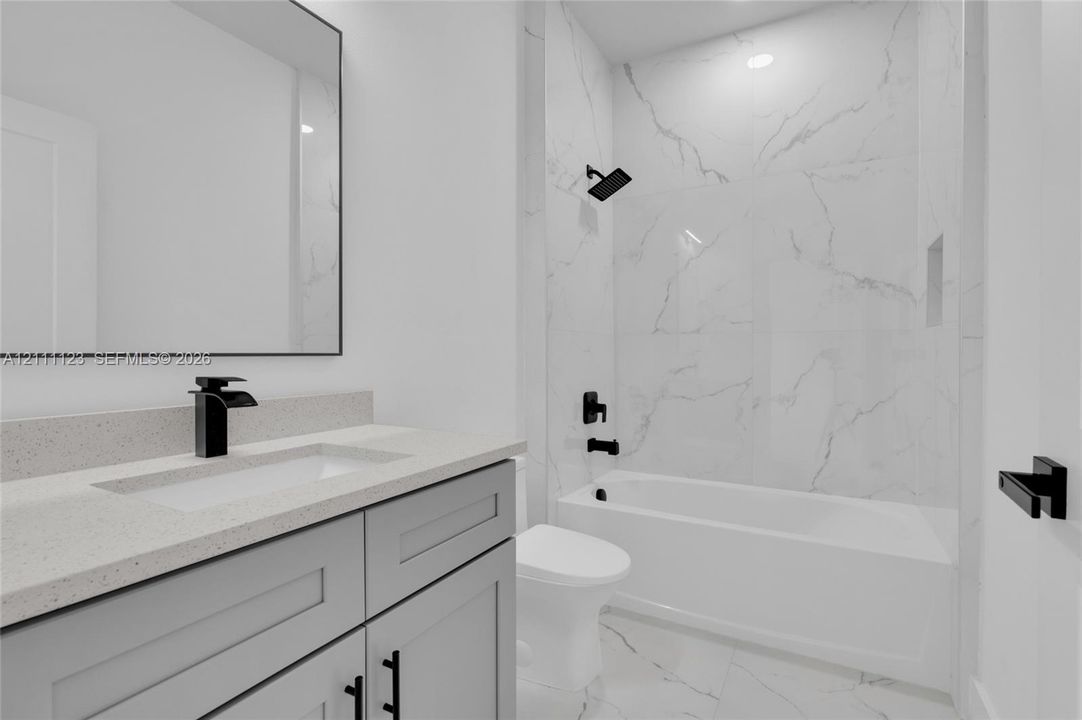 Guest bath with tub and shower combination, quartz-topped gray vanity, and black fixtures.