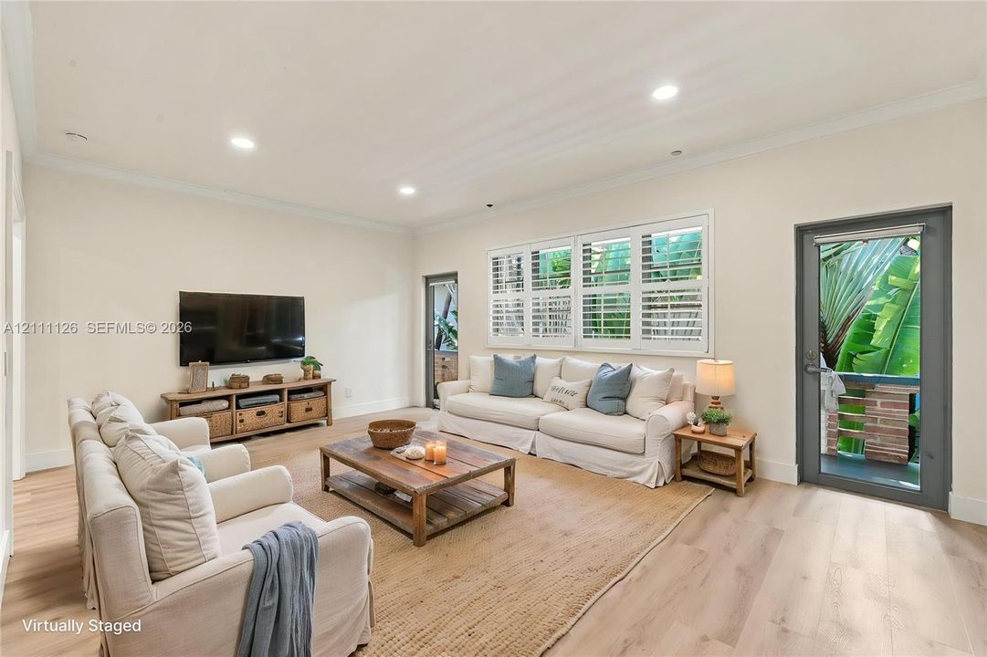 Living area featuring light-toned wood-finish flooring, recessed lighting, crown molding, multi-pane windows with plantation shutters, and two full-lite exterior doors