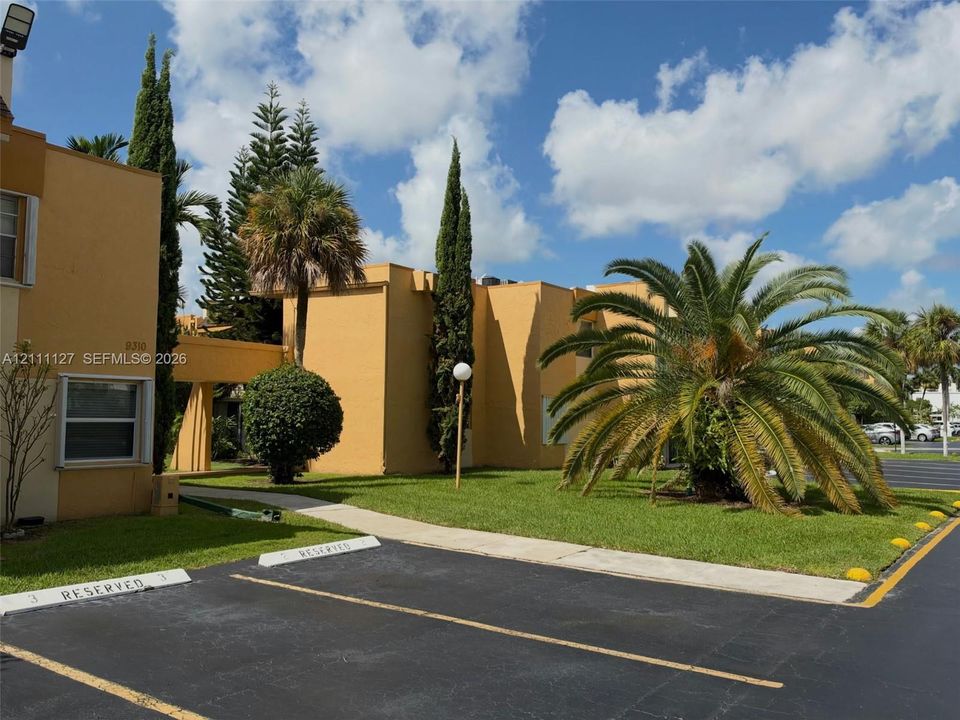 Exterior facade featuring stucco siding, mature landscaping, and assigned parking spaces