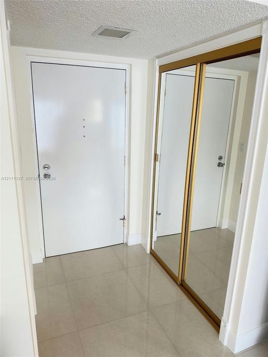 Entryway featuring large-format ceramic floor tiling, a solid core white door with a security viewer, and sliding mirrored closet doors with gold-tone metal frames
