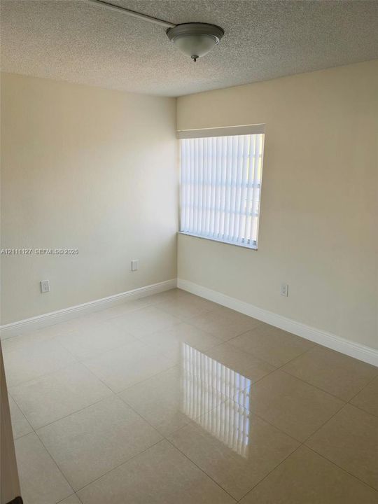 Neutral-toned interior space featuring light-colored large-format tile flooring, textured ceiling, central dome lighting, and vertical window blinds