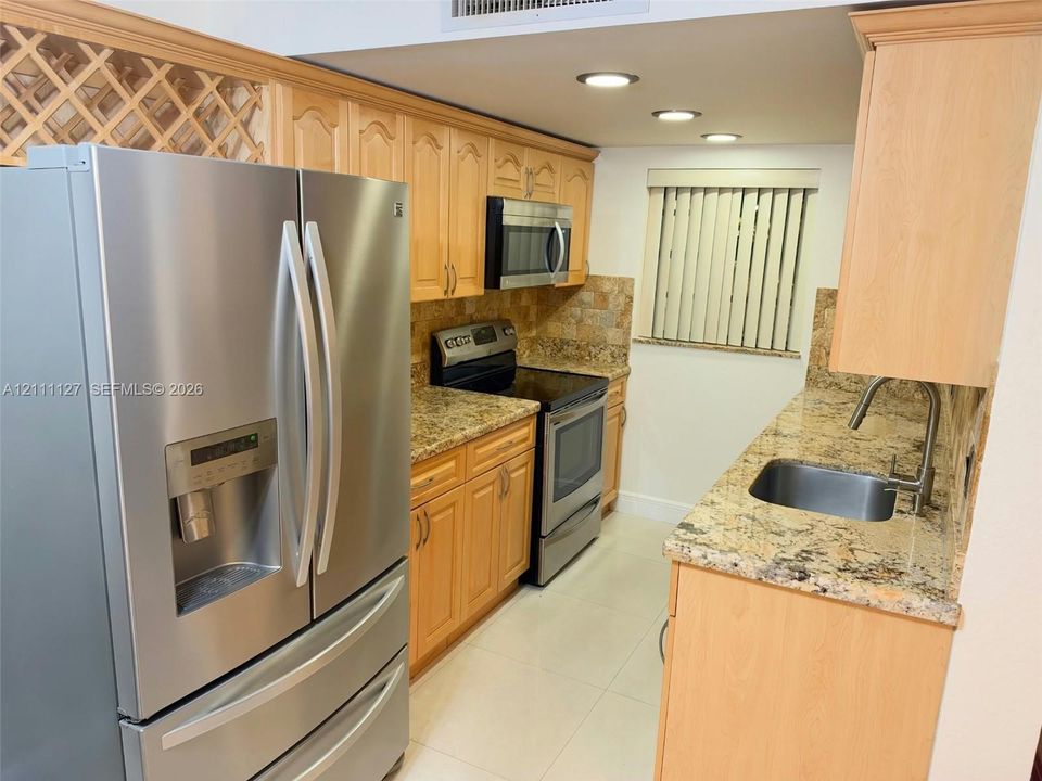Kitchen featuring light-finish wood cabinetry, stone countertops, stainless steel appliances, a built-in wine rack, and recessed ceiling lighting