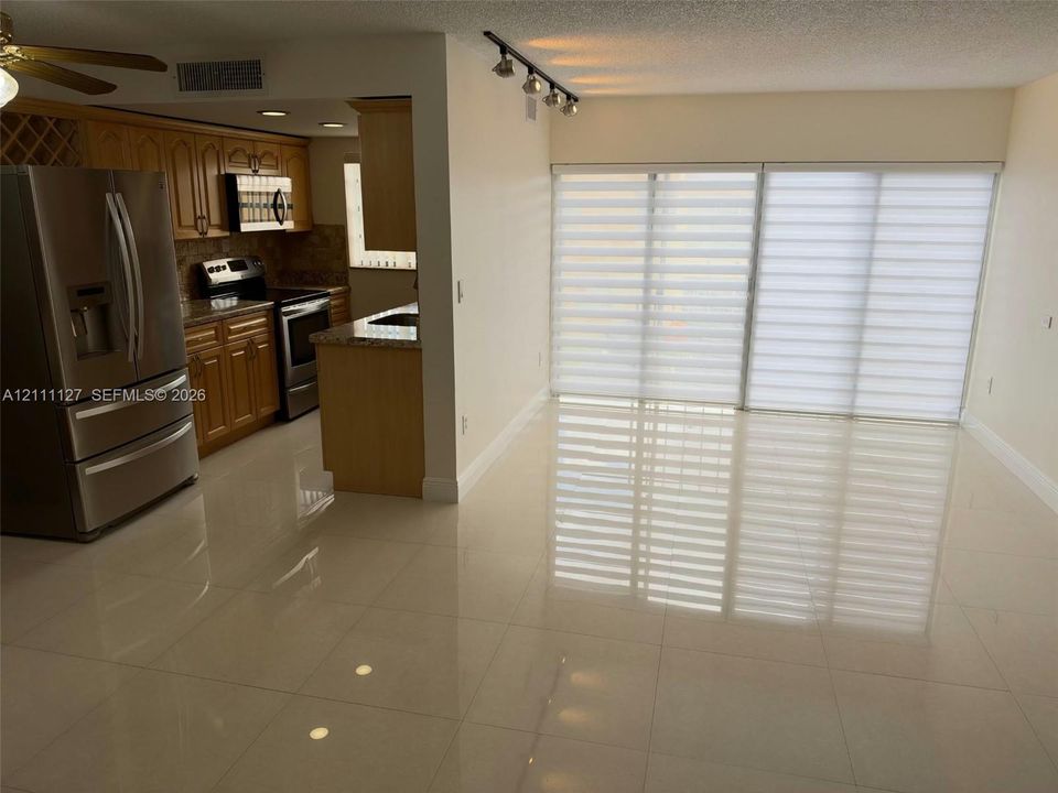 Kitchen featuring wood cabinetry, stone countertops, and stainless steel appliances, paired with large-format tile flooring and sliding glass doors with roller shades