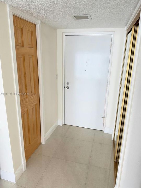 Entryway featuring large-format neutral tile flooring, a solid core white door with security hardware, a six-panel wood-finish interior door, and a mirrored sliding-door closet