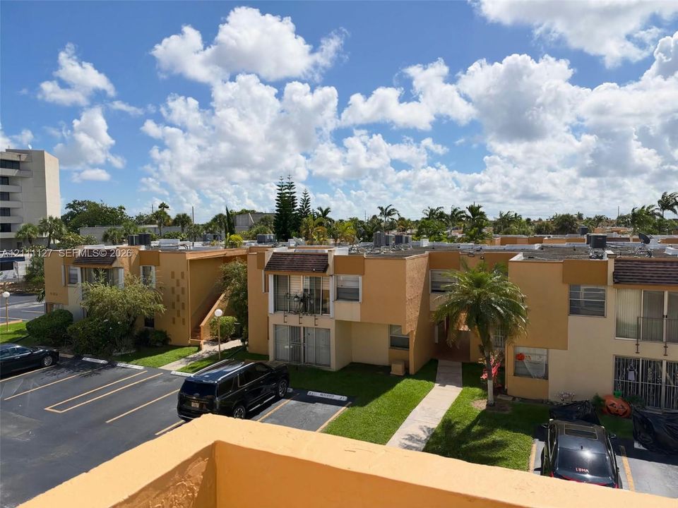 Multi-level residential exterior featuring tan stucco siding, concrete walkways, private balconies, and landscaped grounds