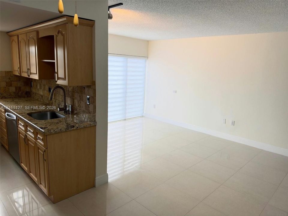 Kitchen featuring wood cabinetry, stone countertops, a stainless steel undermount sink, and a tiled backsplash, complemented by large-format tile flooring