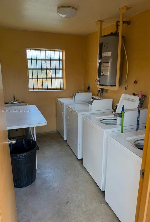 Utility room featuring concrete flooring, a wall-mounted water heater, and a multi-unit laundry configuration