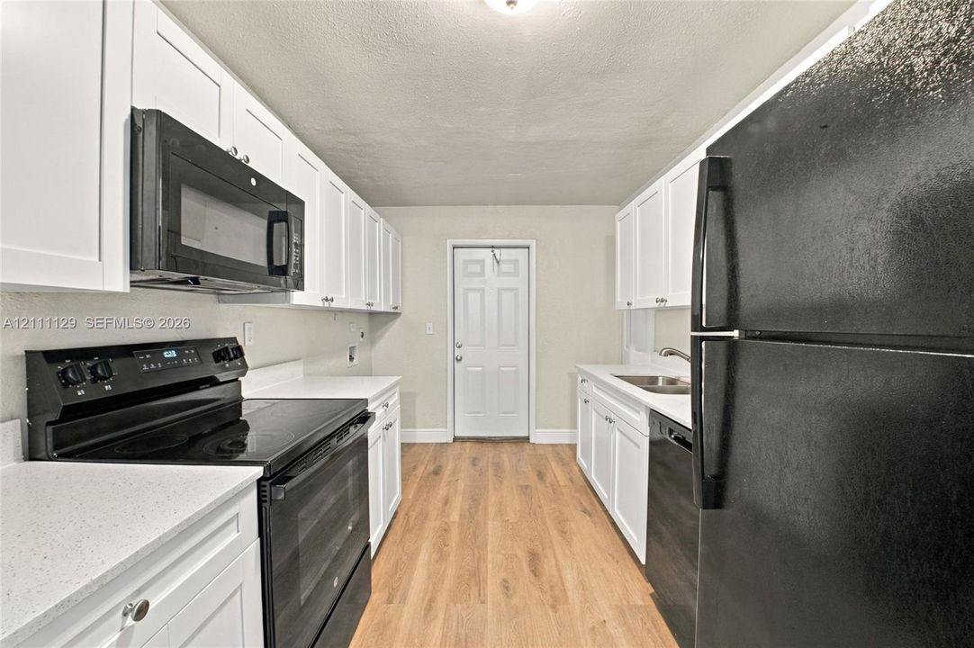 Kitchen featuring white shaker-style cabinetry, light-toned wood-finish flooring, solid surface countertops, and black built-in appliances