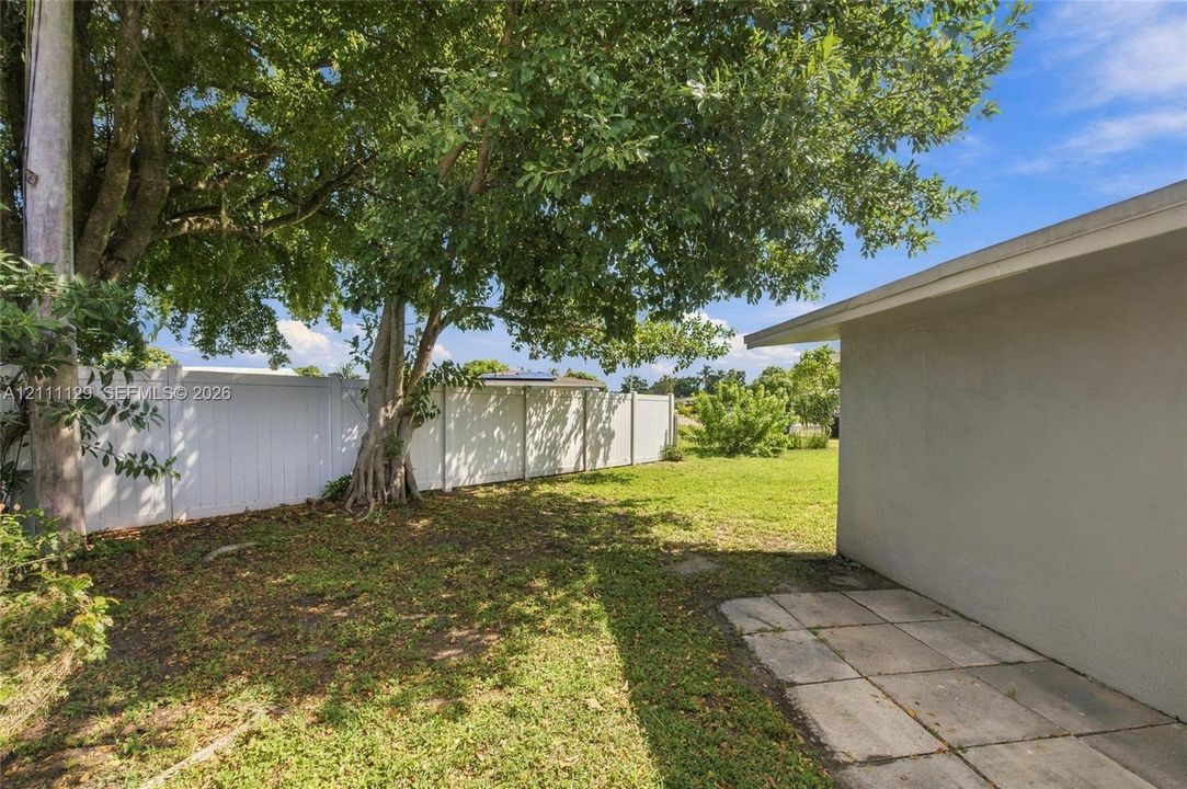 Backyard featuring a concrete paver patio, full-height white vinyl privacy fencing, and mature canopy trees