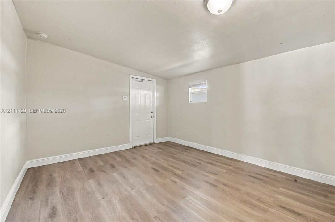 Interior space featuring wood-finish flooring, neutral wall tones, a six-panel door, and a flush-mount ceiling light fixture