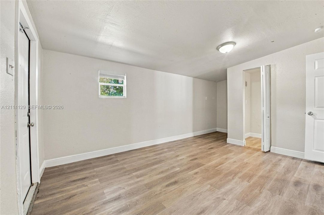 Interior space featuring light-toned wood-finish flooring, neutral wall paint, a flush-mount ceiling light, a single-pane window, and white interior doors