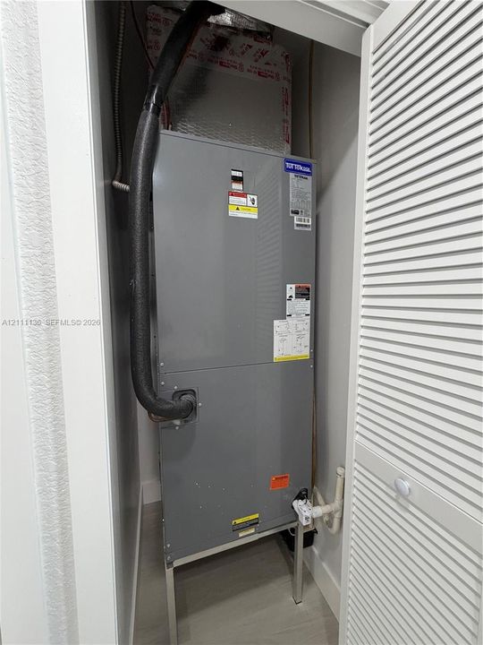 Utility closet housing a vertical HVAC air handler unit with insulated ductwork and a louvered door enclosure