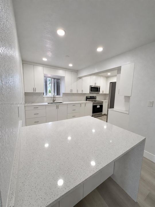 Kitchen featuring white shaker-style cabinetry, quartz countertops, a waterfall-edge island, stainless steel appliances, and recessed lighting