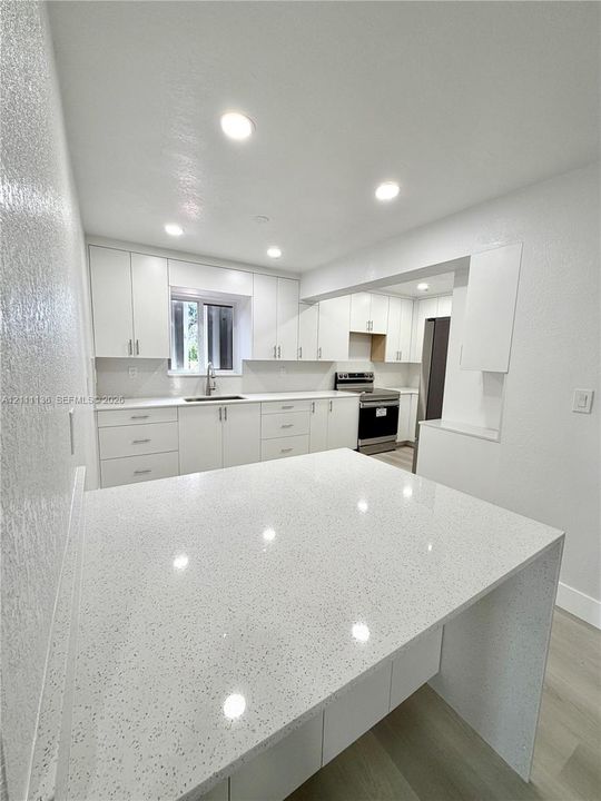Kitchen featuring white cabinetry, quartz countertops with a waterfall edge, recessed lighting, and wood-finish flooring