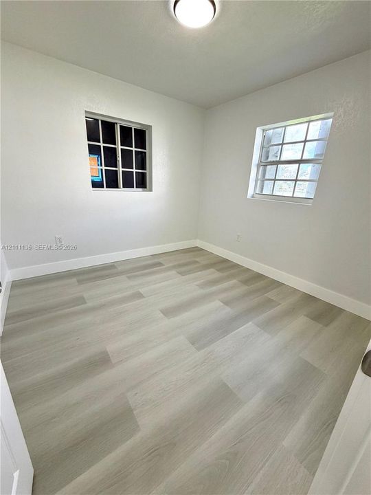 Neutral-toned room featuring wood-finish flooring, white walls, two grid-pane windows, and a flush-mount ceiling light fixture