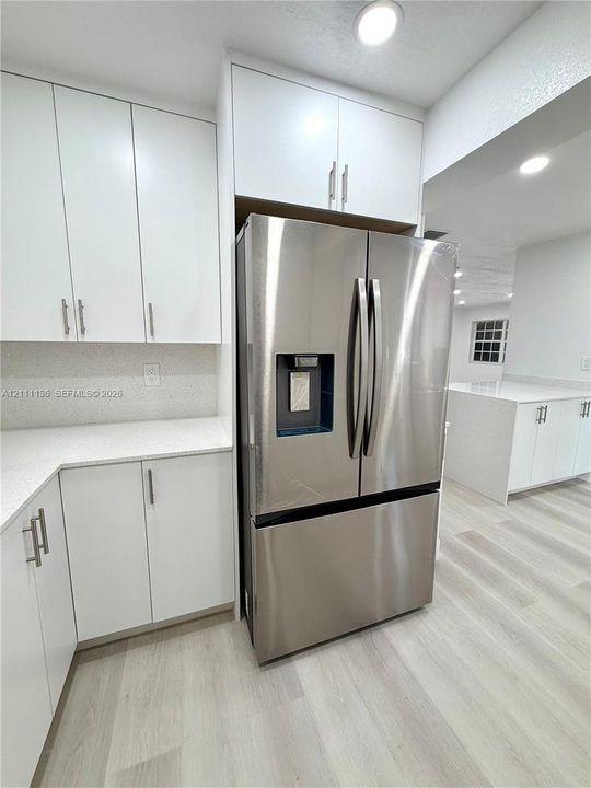 White shaker-style cabinetry with satin nickel pulls, stone-composite countertops, stainless steel French door refrigerator, and wood-finish flooring