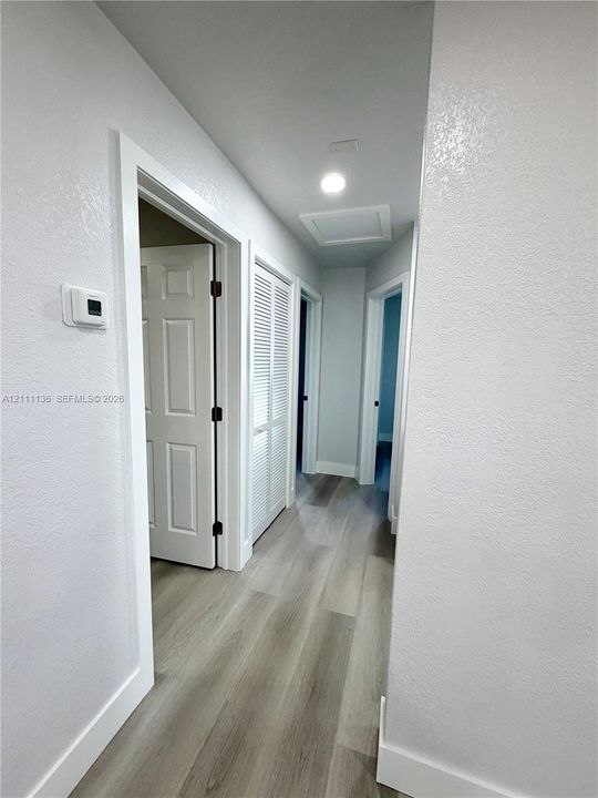 Hallway featuring wood-finish flooring, recessed ceiling lighting, louvered bi-fold doors, and multi-panel interior doors