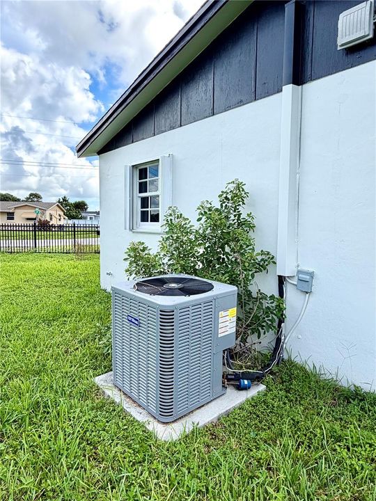 Exterior profile featuring a white stucco facade, dark-toned vertical siding, a single-hung window with shutters, and an external HVAC condenser unit on a concrete pad