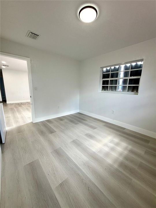 Neutral-toned wood-finish flooring, crisp white walls, flush-mount ceiling lighting, and multi-pane horizontal window