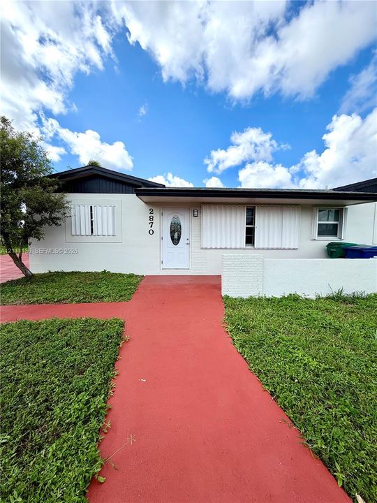 Single-story exterior featuring a white stucco facade, painted concrete walkway, louvered window shutters, and a white front door with an oval glass insert