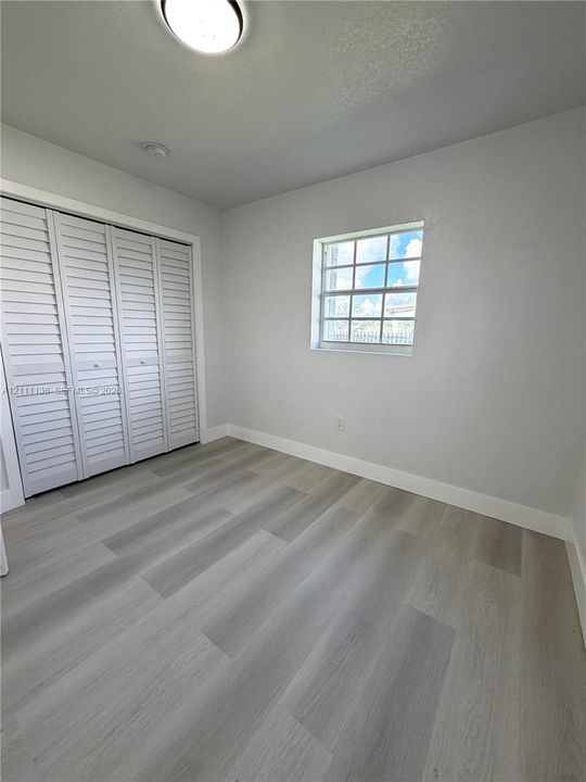 Neutral interior space featuring wood-finish flooring, louvered-style bi-fold closet doors, and a grid-pane window with a flush-mount overhead light fixture