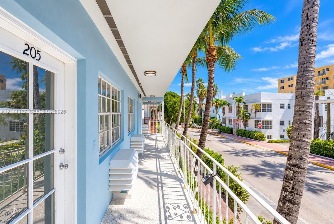Exterior walkway featuring a painted stucco finish, multi-lite glass panel door, terrazzo flooring, metal lattice railing, and overhead recessed lighting
