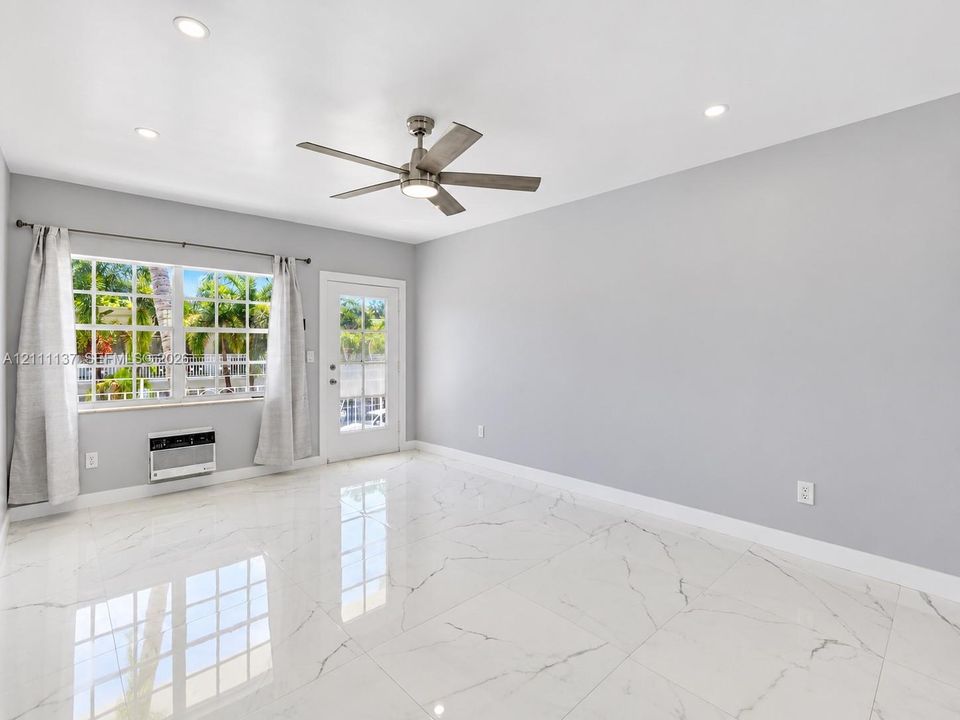 Large-format tile flooring with polished finish, recessed ceiling lighting, brushed metal ceiling fan with integrated lighting, multi-pane window, and exterior door with glass insert