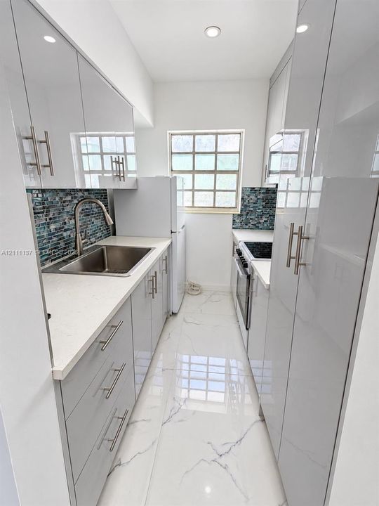 Kitchen featuring high-gloss cabinetry, stone-surface countertops, blue mosaic tile backsplash, stainless steel sink with gooseneck faucet, and large-format porcelain tile flooring